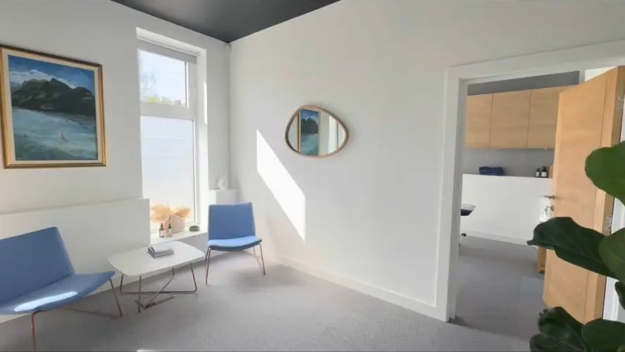 Light-filled osteopathy clinic in Queen’s Park with blue chairs and a full-length mirror